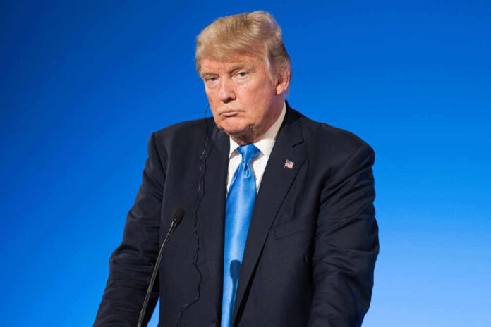 shutterstock_677261236.jpg featured image Donald Trump in suit with blue background speaking at podium.