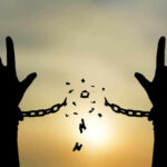 Silhouetted hands breaking chains against sunset sky.