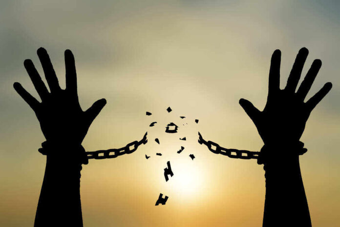 shutterstock_703687810.jpg featured image Silhouetted hands breaking chains against sunset sky.