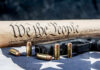 Gun, bullets, Constitution scroll on American flag.