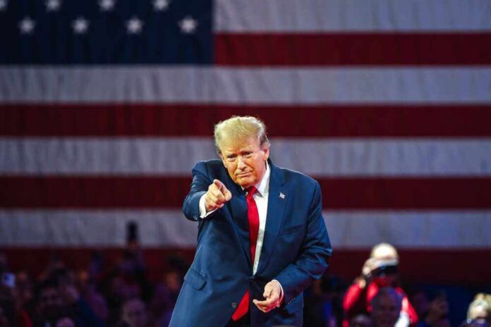 shutterstock_2455396913-1.jpg featured image Donald Trump in front of American flag pointing toward camera.