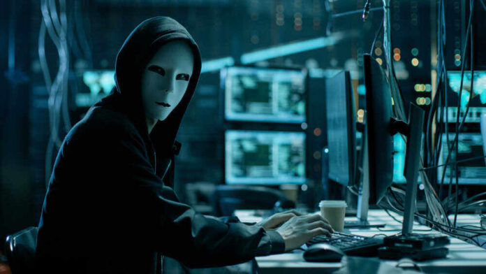 shutterstock_680078920.jpg featured image Person in hoodie and mask using computer, multiple screens.