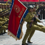 Soldiers marching with rifles and a flag banner