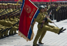 Soldiers marching with rifles and a flag banner