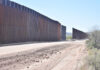 Dirt road beside tall metal border wall