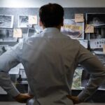 Man examining investigation board with photos and notes.