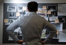 Man examining investigation board with photos and notes.