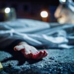 Crime scene with covered body and hand exposed.