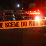 Crime scene tape with emergency vehicles in background