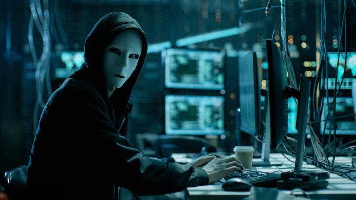 Person in hoodie and mask using computer, multiple screens