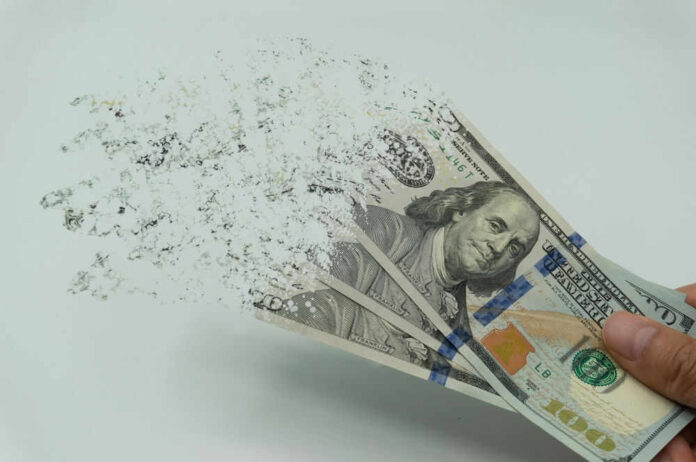 shutterstock_2122253927.jpg Hundred-dollar bills disintegrating in hand.