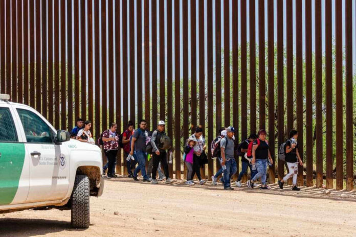 Group of people walking by a border fence.