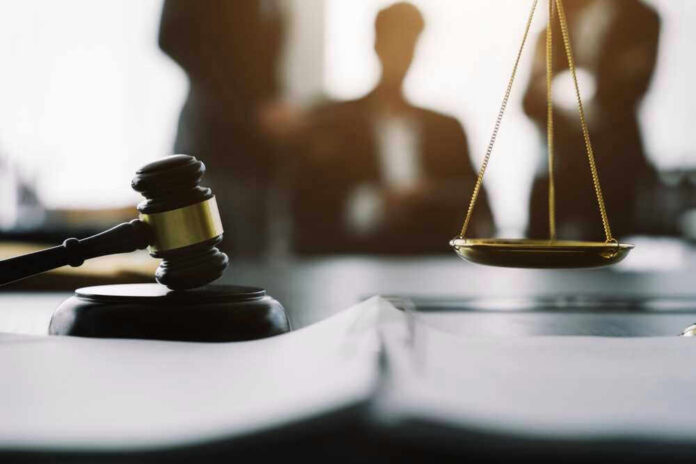Gavel and scales in courtroom with blurred figures behind.