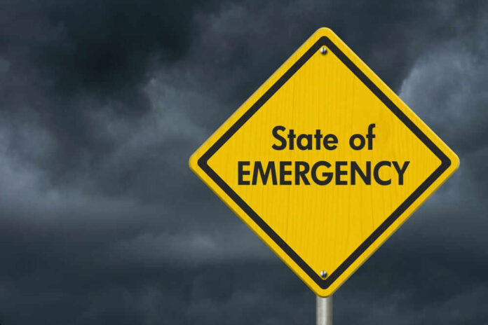 shutterstock_2264564769.jpg Yellow warning sign reading State of Emergency