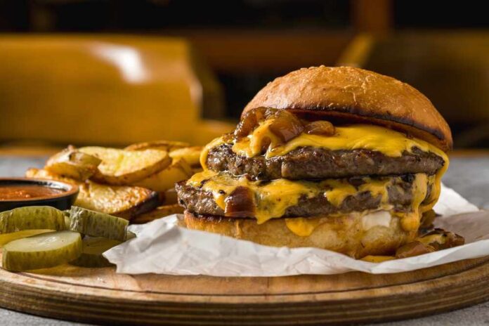 A double cheeseburger with melted cheese and pickles served with potato wedges
