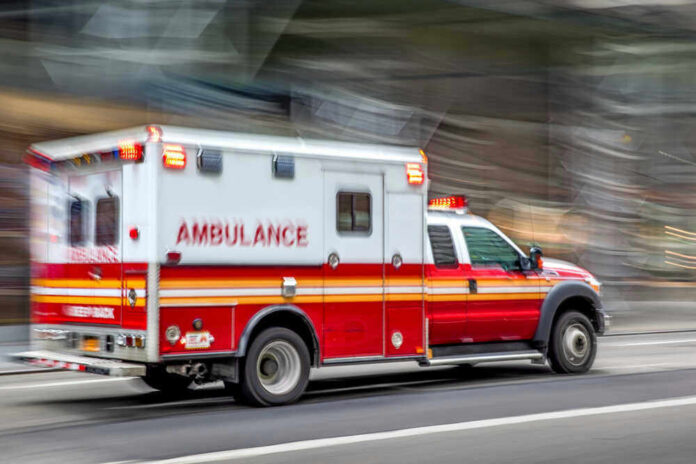shutterstock_1495131698.jpg Red and white ambulance driving on a city street.