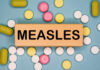 Wooden block with the word 'MEASLES' surrounded by various pills