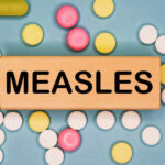 Wooden block with the word 'MEASLES' surrounded by various pills