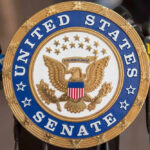 United States Senate seal with microphones in front.