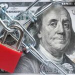 Trump’s New CRACKDOWN — Funds FROZEN! A red padlock and chain over a hundred dollar bill featuring Benjamin Franklin