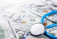 A stethoscope resting on a pile of hundred-dollar bills