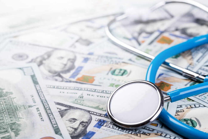 A stethoscope resting on a pile of hundred-dollar bills