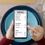 A person holding a smartphone displaying a restaurant menu with various food items