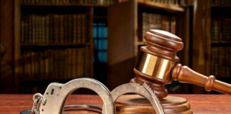 Wooden gavel and handcuffs on a table.