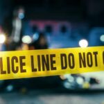 Police line caution tape at a crime scene with blurred figures in the background