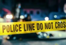 Police line caution tape at a crime scene with blurred figures in the background