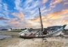An abandoned boat on a sandy shore during sunset