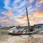 An abandoned boat on a sandy shore during sunset