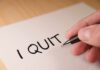 A hand writing 'I QUIT' on a piece of paper