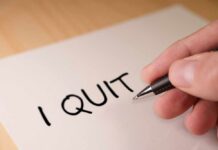 A hand writing 'I QUIT' on a piece of paper