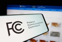 Close-up of a mobile device displaying the FCC logo with a website in the background
