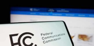 Close-up of a mobile device displaying the FCC logo with a website in the background
