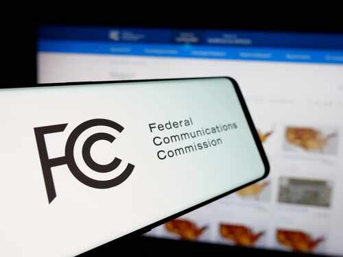 Close-up of a mobile device displaying the FCC logo with a website in the background