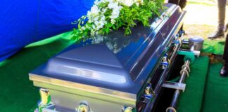 A silver casket adorned with flowers at a gravesite