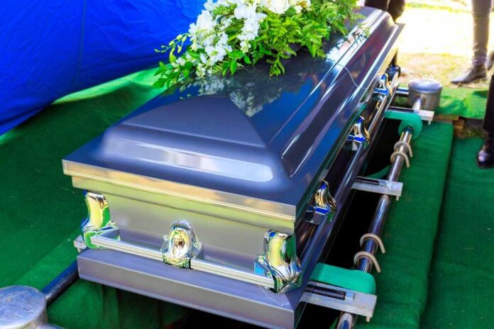 A silver casket adorned with flowers at a gravesite