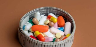 A bowl filled with various colorful pills and capsules next to a measuring tape