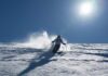 Skier carving through fresh snow under a clear blue sky