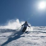Skier carving through fresh snow under a clear blue sky