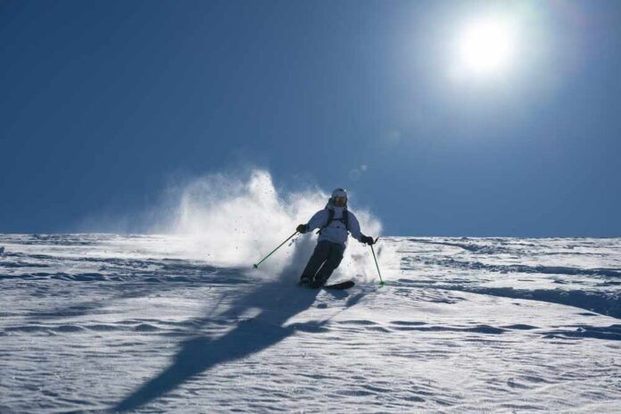 Skier carving through fresh snow under a clear blue sky