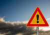 A triangular warning sign with an exclamation mark against a cloudy sky
