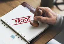 A hand holding a wooden stamp over a document marked 'PROOF'