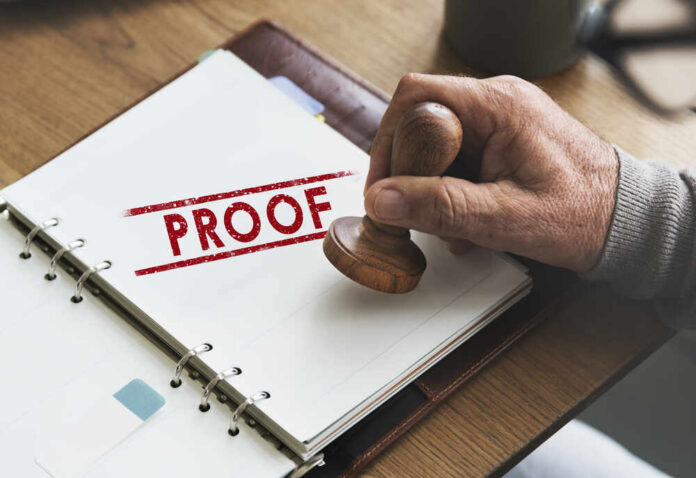 A hand holding a wooden stamp over a document marked 'PROOF'