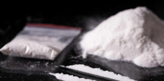 A bag of white powder next to two lines of powder on a reflective surface