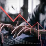 Person typing on a laptop with a declining stock market graph overlay