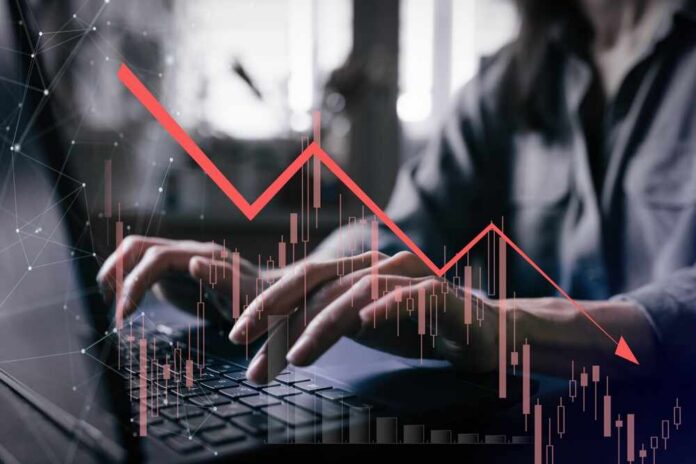 Person typing on a laptop with a declining stock market graph overlay