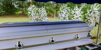 A casket at a graveside surrounded by floral arrangements